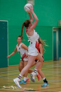 Lizzie playing netball, jumping with the ball to shoot