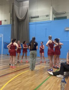 Photo of Lizzie and her netball team on the court, holding a meeting