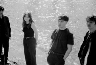 A black and white image of four people stood on the beach