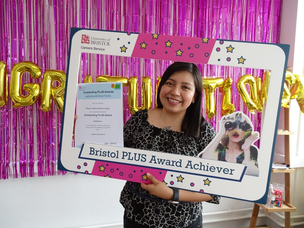 An image of a student smiling behind a selfie frame labelled "Bristol PLUS Award achiever"