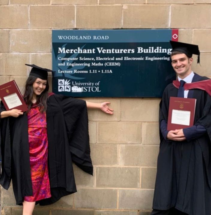 A picture of a man and a woman in graduation gowns, outside of University.
