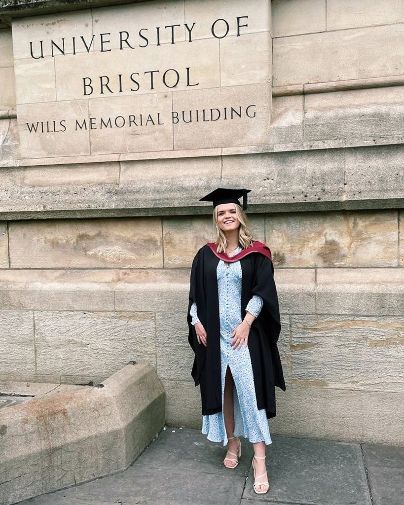 Emma, in her graduate gown, smiling outside Wills memorial Building 