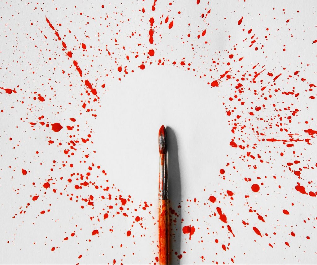A paintbrush covered in red paint surrounding by a circular splatter pattern on a white background.