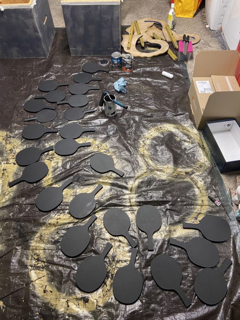 A photo of wooden paddles being painted black.
