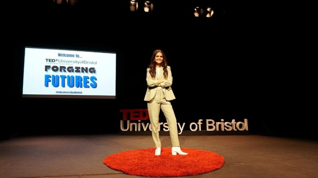 A woman, Maya Raichoora, standing presenting on a stage.