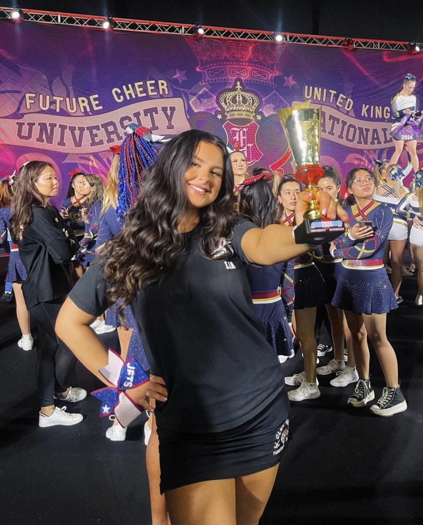 Lia in Cheer uniform holding up a trophy