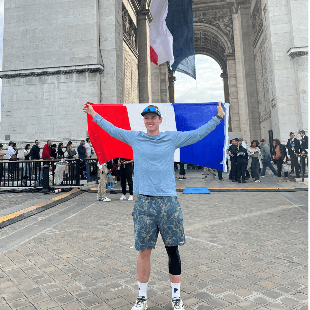 A photo of Lucca holding the French flag high, wearing a supportive knee bandage. It looks like he's in France.