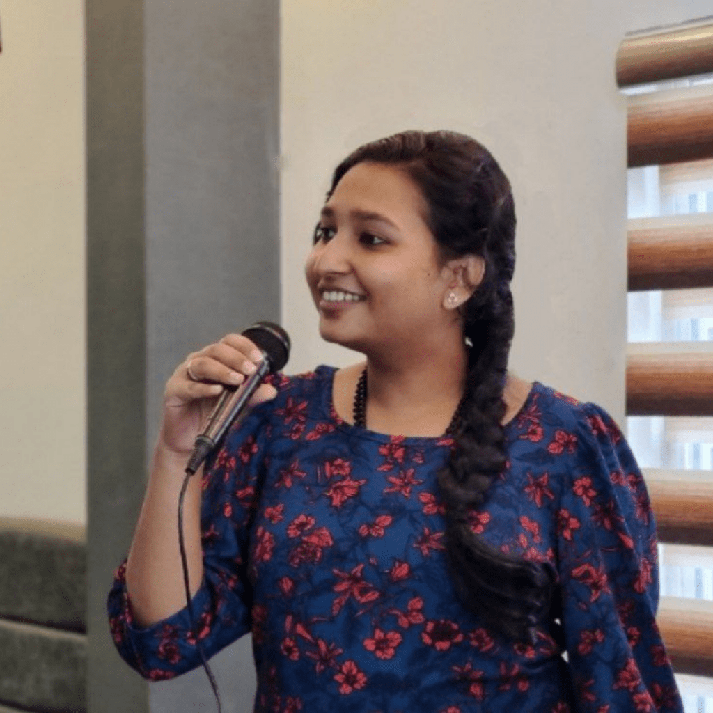 A photo of Rajasree speaking into a microphone at an event.