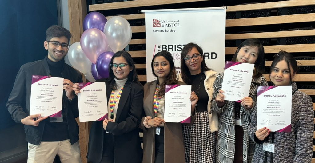A group of students proudly showing off their PLUS Award certificates. They are standing in front of balloons and a PLUS Award banner.